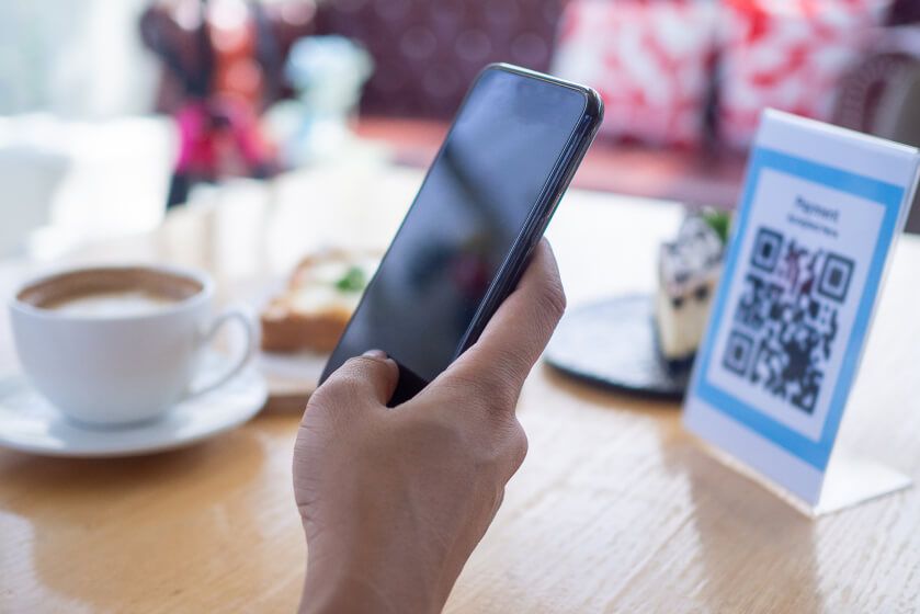FAQ Imagem de uma pessoa utilizando o seu celular para ler um QR Code.